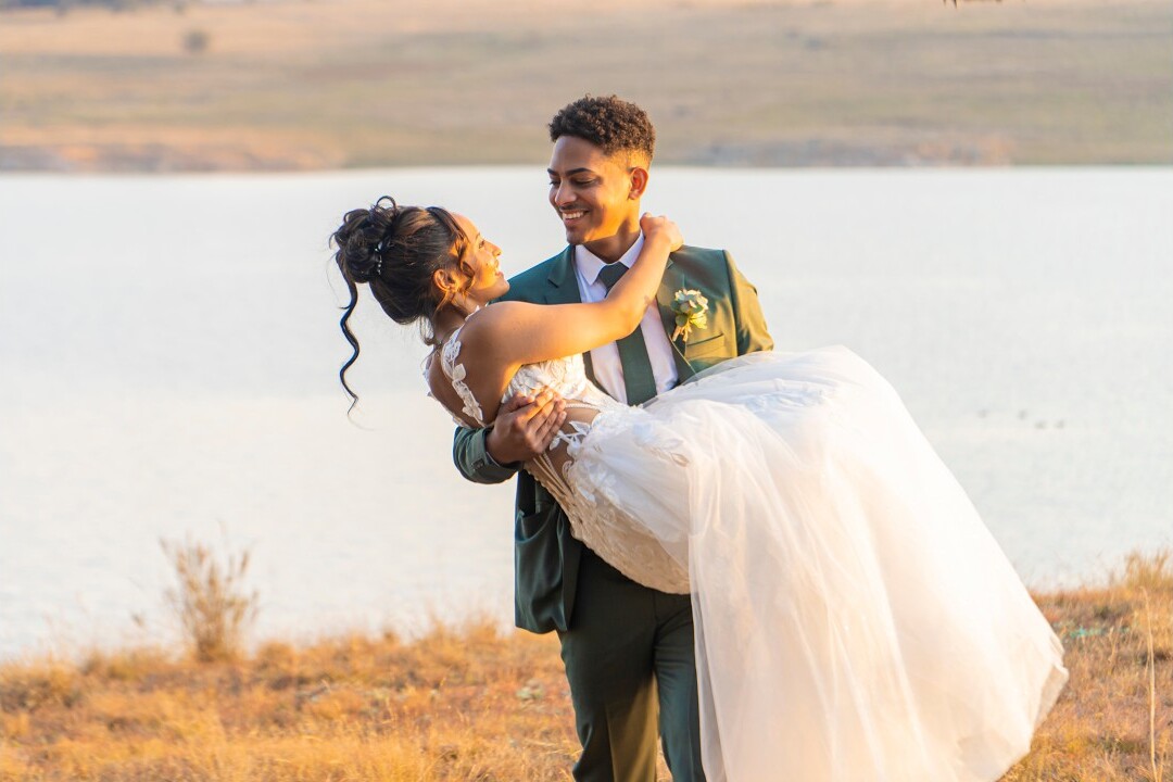 Frame from a wedding film: groom lifting his bride beside the water
