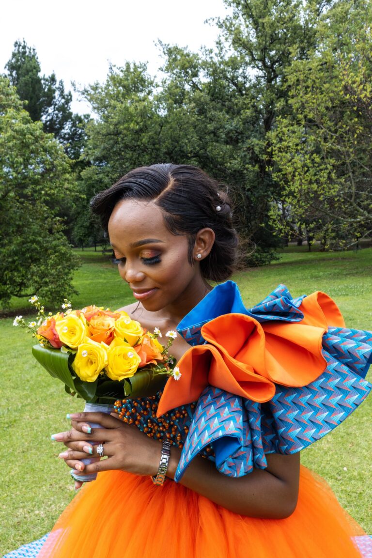 Bride looking down at her bouquet, with a ruffled blue and orange shoulder
