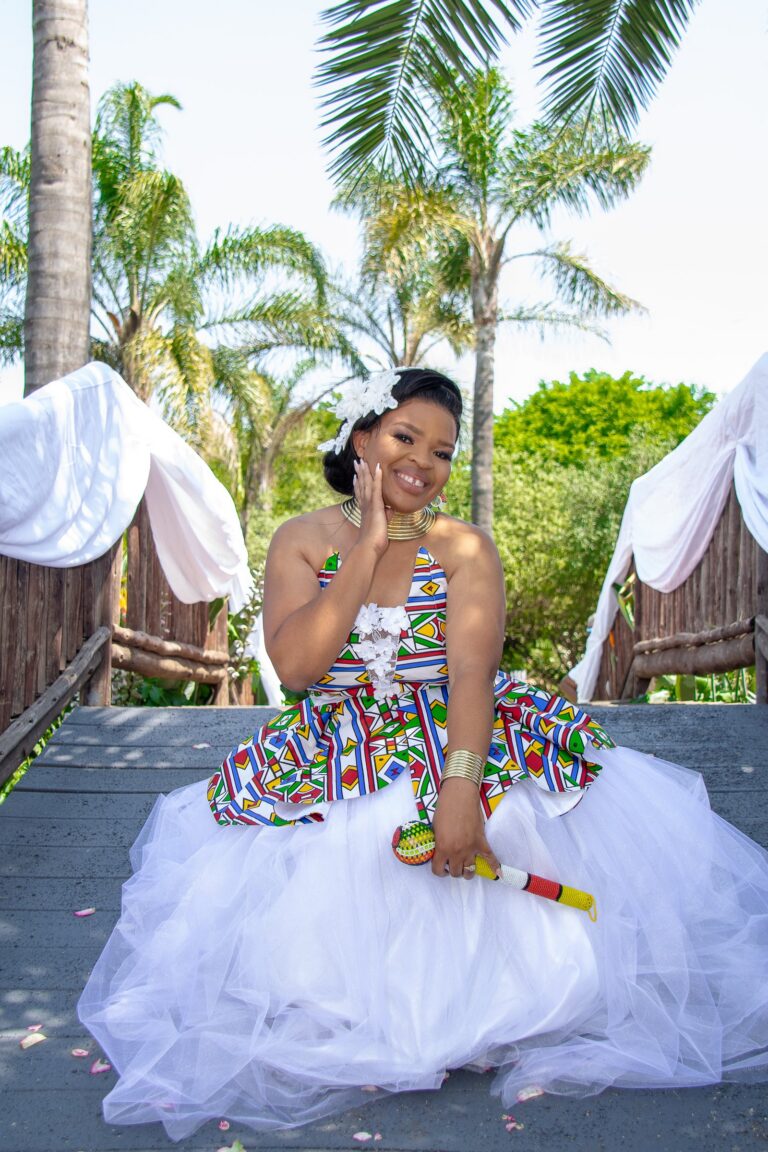 Bride seated on a wooden bridge in a white gown with a bright geometric bodice