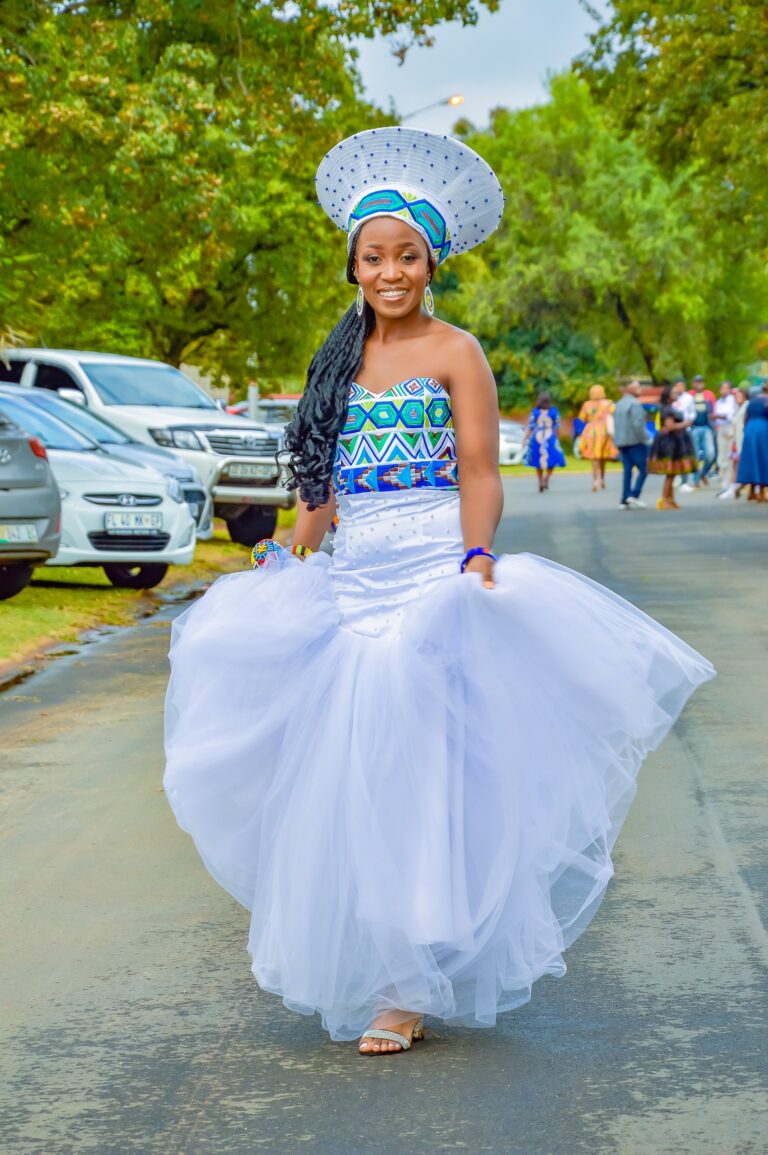 Bride in a beaded headdress walking to the celebration as guests gather behind her