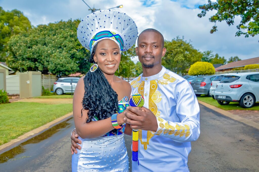 Couple holding a beaded staff together, the bride in a wide beaded headdress