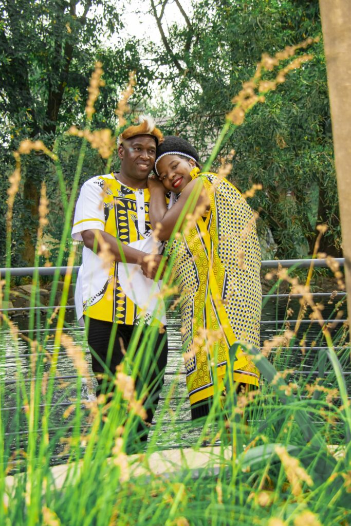 Couple in yellow and black traditional attire embracing beside a pond