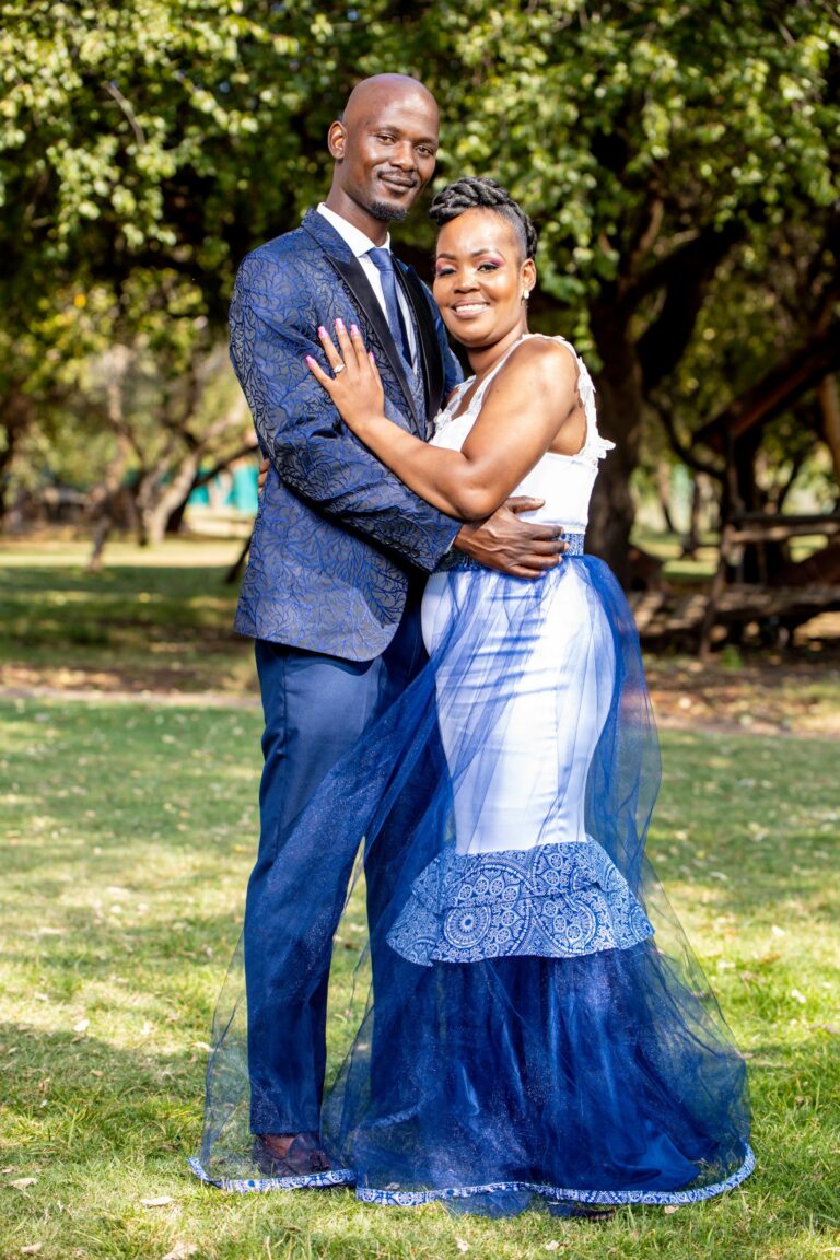 Couple embracing under trees, the bride in a white and blue gown