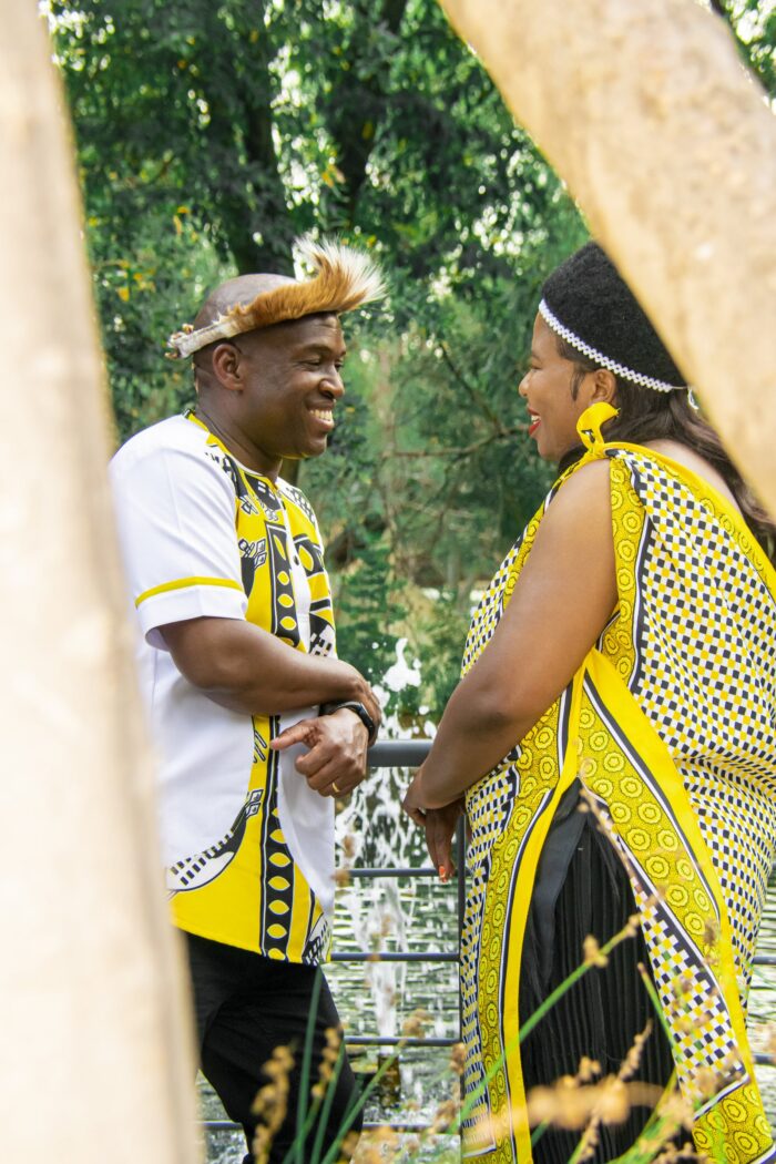 Couple in yellow and black traditional attire laughing together in a garden