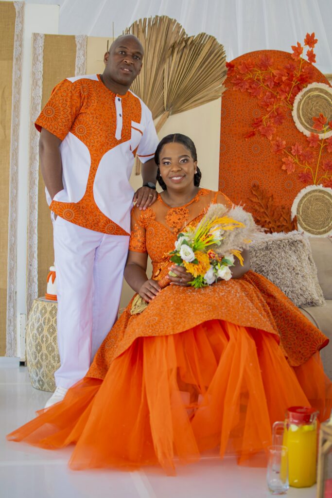 Couple in orange and white attire posed in front of their decorated stage