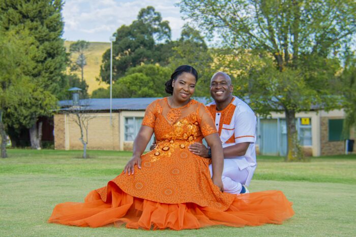 Couple in matching orange and white traditional attire seated together on a lawn