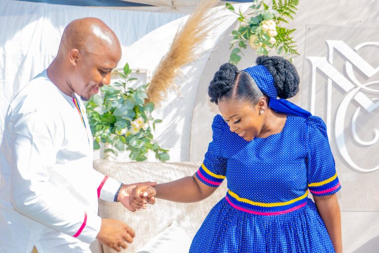 Groom taking his bride's hand as she laughs, in a blue traditional dress