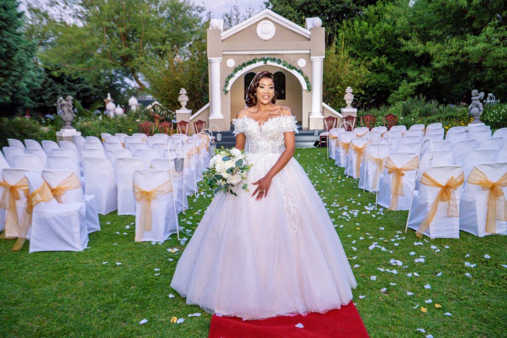 Bride standing on a red carpet aisle in front of a garden chapel