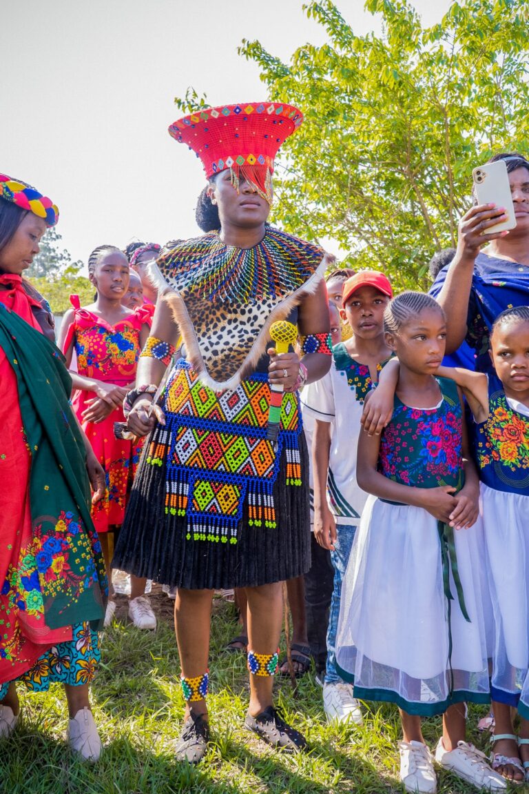 Bride in beaded traditional attire and a red headdress surrounded by children