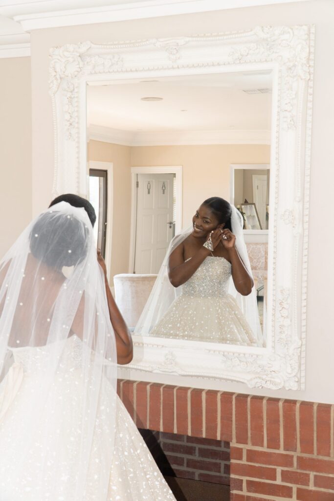 Bride in a beaded gown and veil looking into a mirror while getting ready