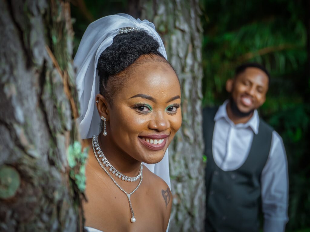 Bride smiling beside a tree with her groom behind her