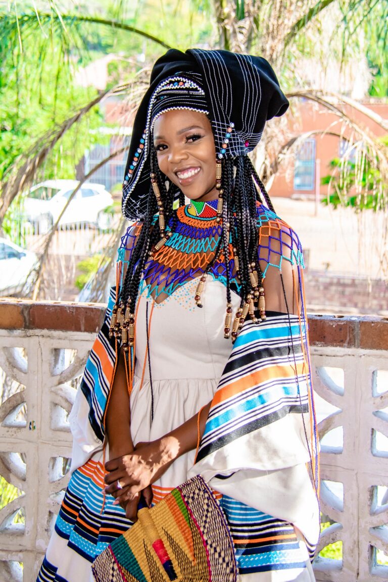Bride in a striped headwrap and beaded necklace smiling on a veranda