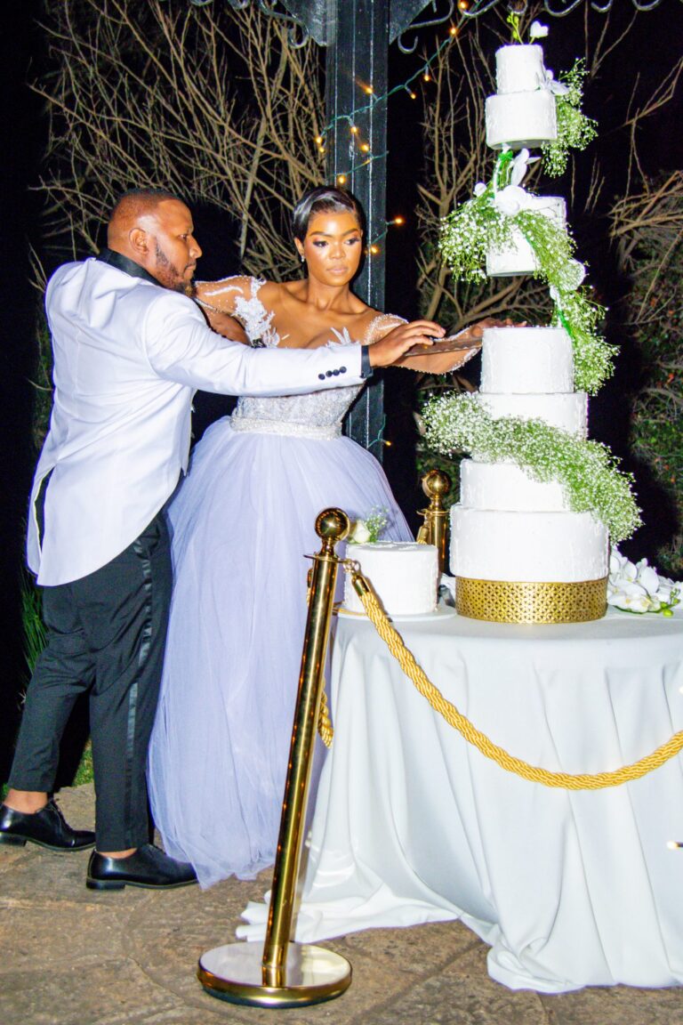 Couple cutting a tall wedding cake in the evening