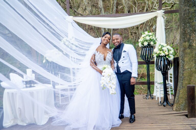 Couple standing under a draped arch as the veil sweeps across the frame