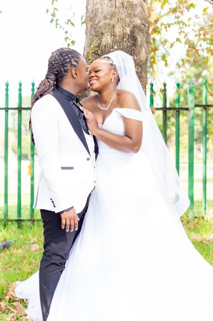 Groom kissing his bride on the cheek beside a tree