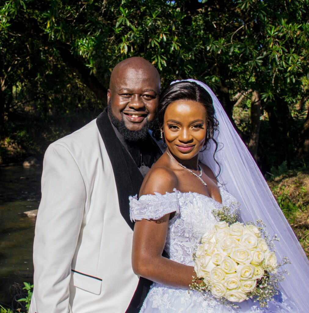 Bride and groom posing together, the bride holding white roses