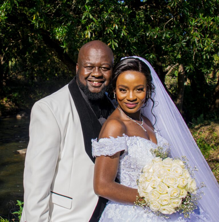 Bride and groom posing together, the bride holding white roses