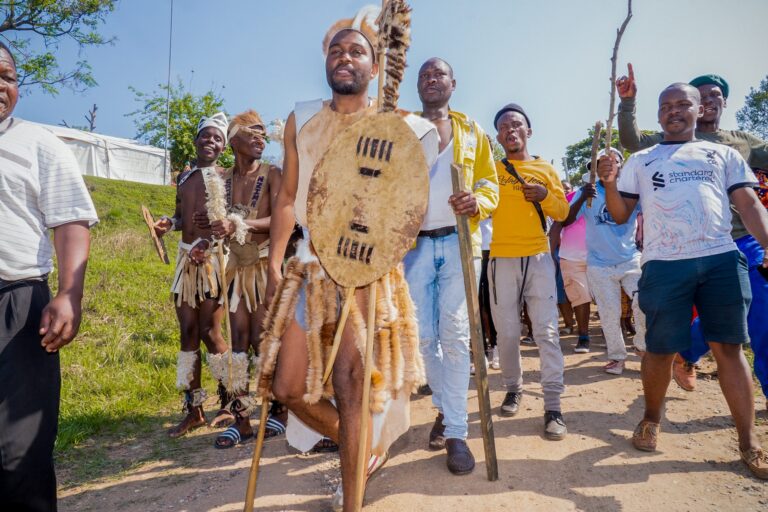 Groom carrying a cowhide shield as he leads a singing procession