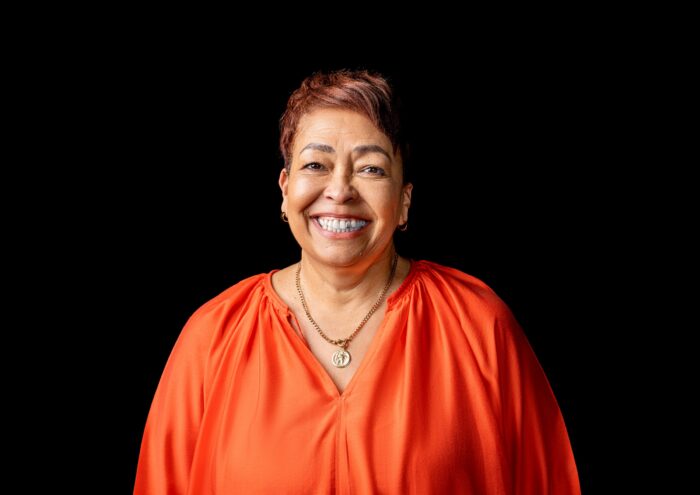 Professional headshot, orange blouse, big smile on a black backdrop, by Studio24.7