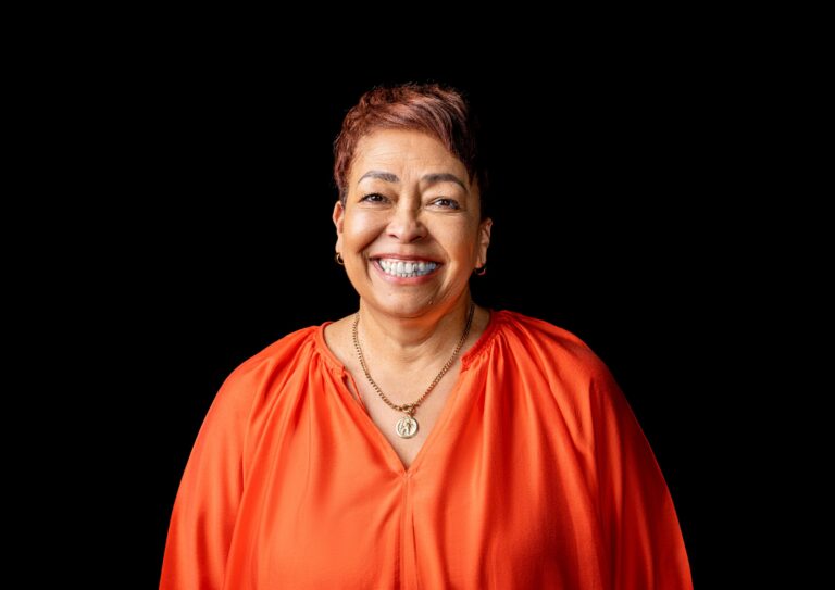 Professional headshot, orange blouse, big smile on a black backdrop, by Studio24.7