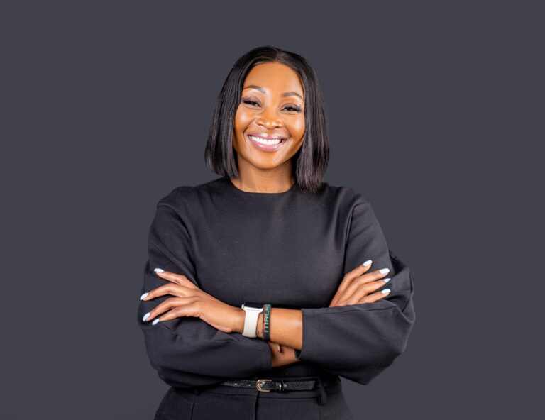 Professional headshot, black top, arms crossed, bright smile on a charcoal backdrop, by Studio24.7