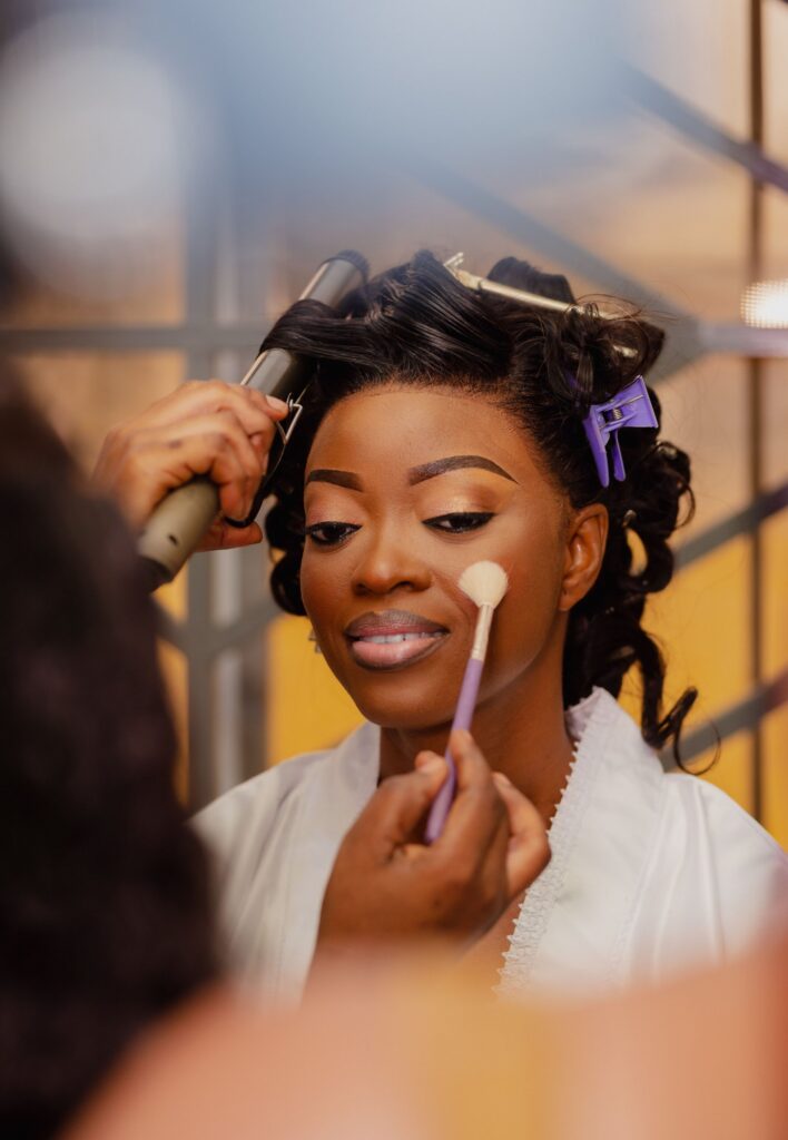 Bride having blush applied with a brush while her hair is curled